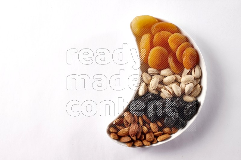 Mixed nuts and dried fruits in a crescent pottery plate on white background