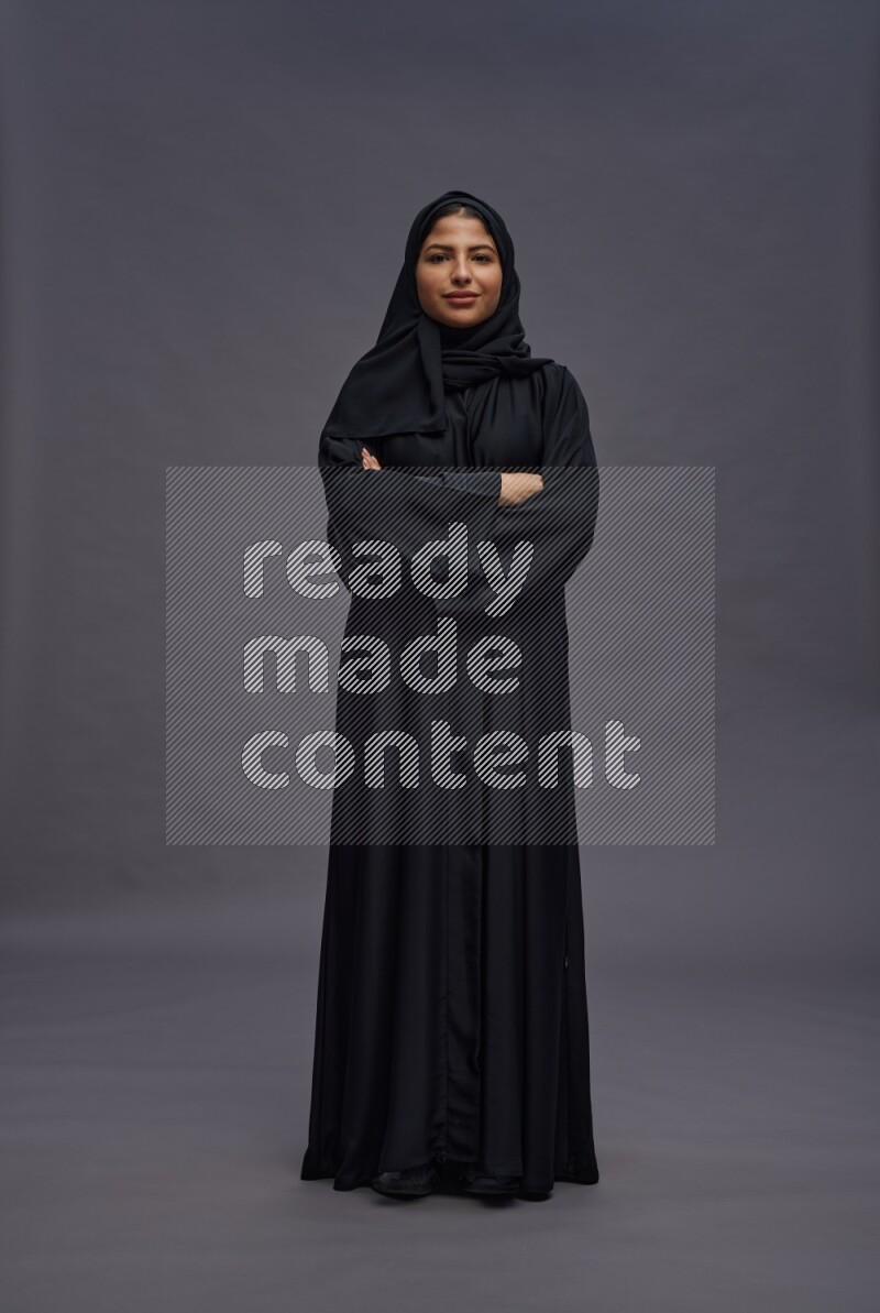 Saudi woman wearing Abaya standing with crossed arms on gray background