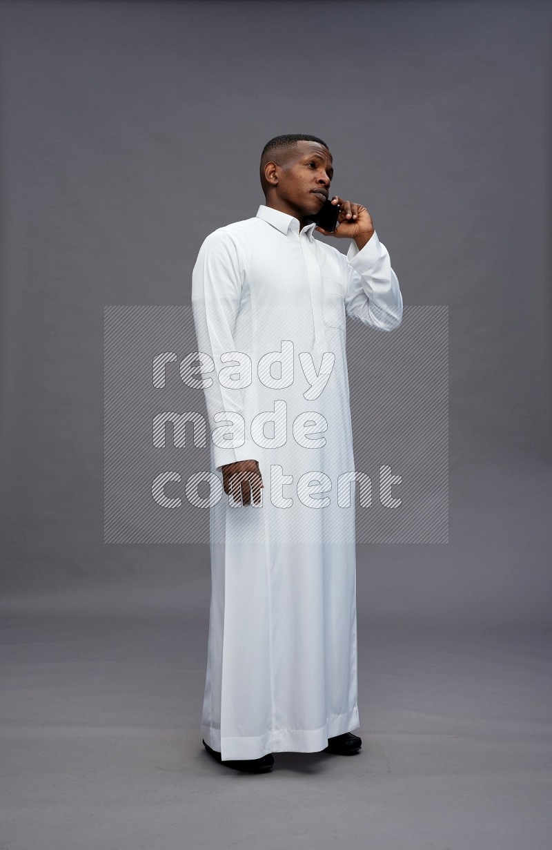 Saudi man wearing thob standing talking on phone on gray background