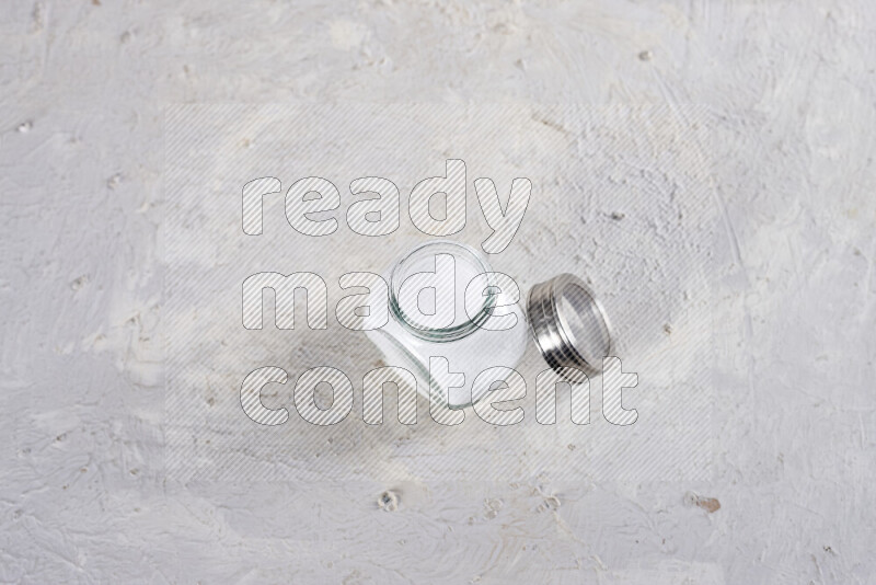 A glass jar full of fine table salt on white background