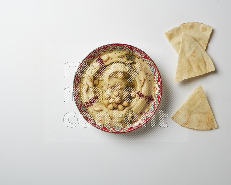 Hummus in a red plate with patterns garnished with zaatar & sumak on a white background