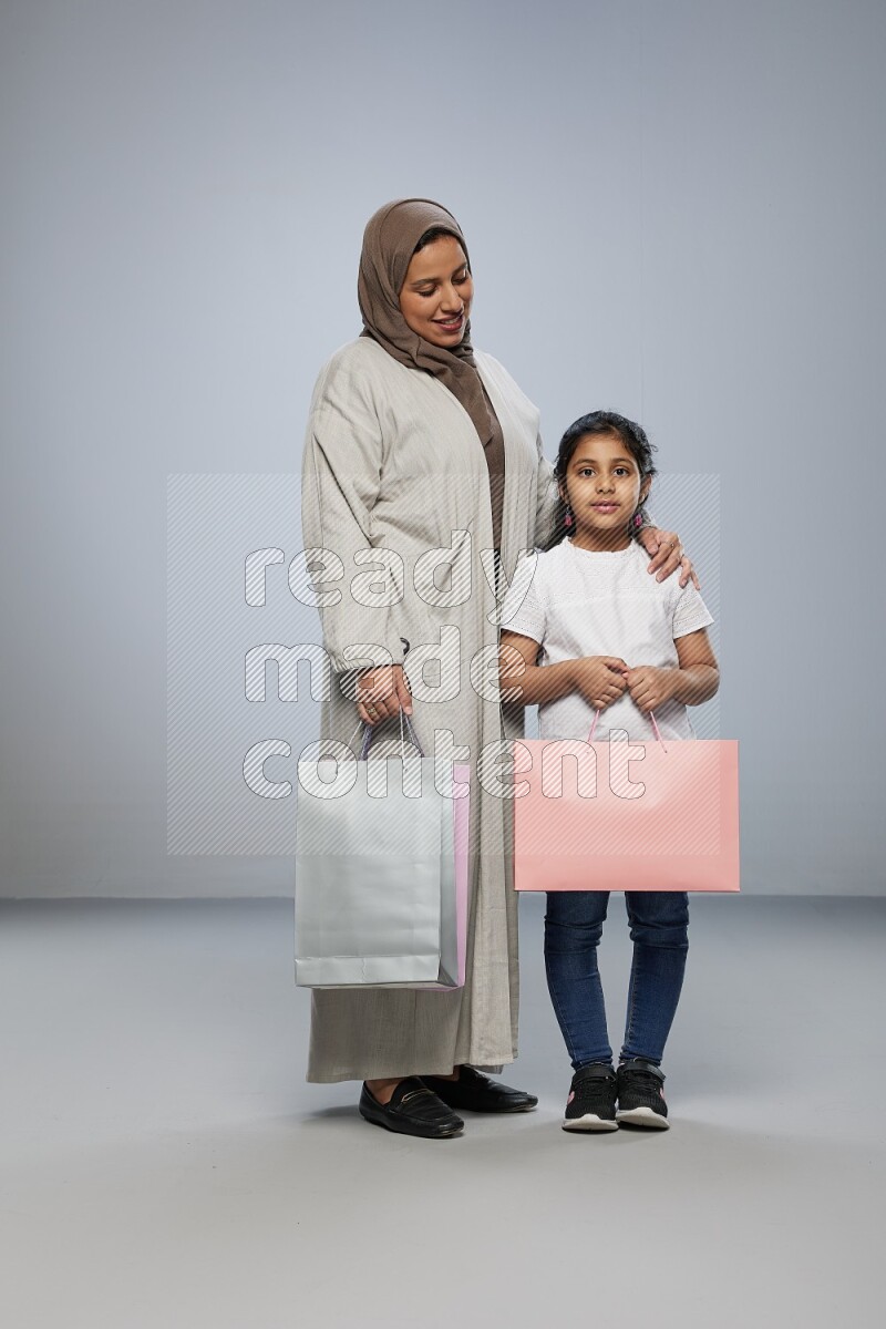 Mom and daughter holding shopping bags on gray background