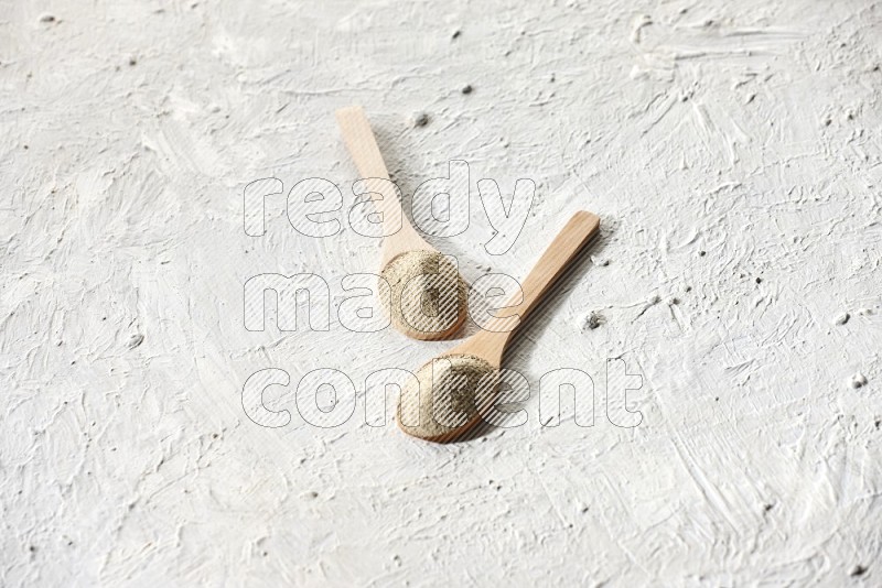 2 wooden spoons full of white pepper powder on textured white flooring