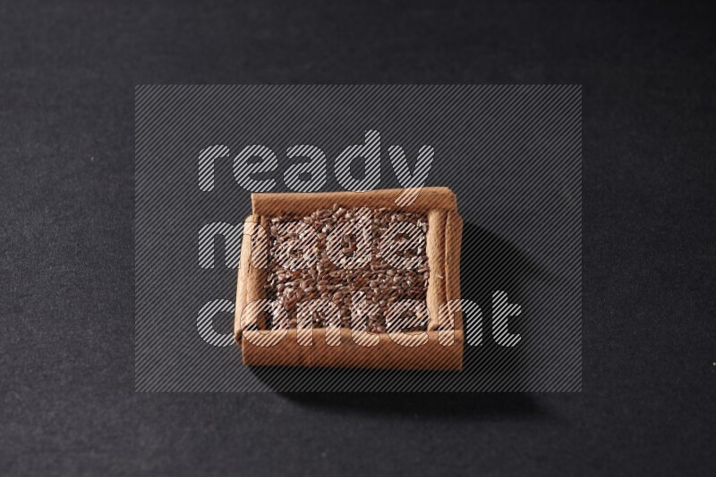 A single square of cinnamon sticks full of flaxseeds on black flooring