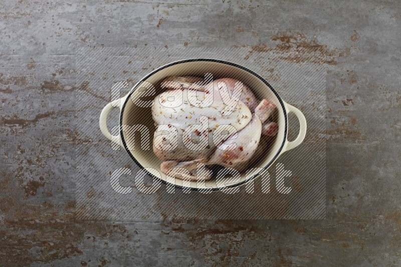 whole raw chicken on in a white ceramic pot direct on a rustic grey background