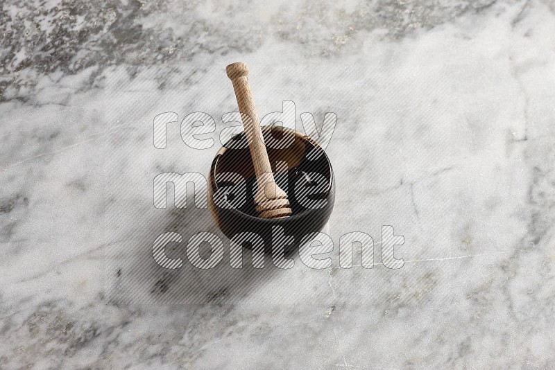 Multicolored Pottery bowl with wooden honey handle in it, on grey marble flooring, 65 degree angle