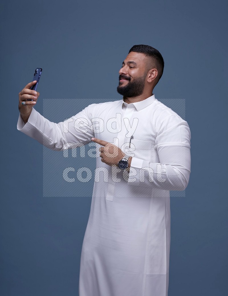 A Saudi man Taking A Selfie on Blue Background wearing Saudi Thob