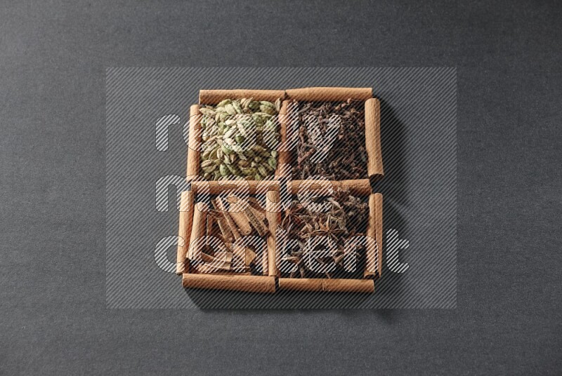 4 مربعات من عيدان القرفة ممتلئة بقطع القرفة وحبوب الهيل والقرنفل اليانسون النجمي على أرضية سوداء