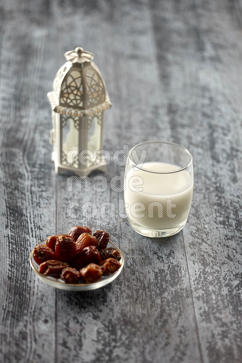 A white lantern with drinks, dates, nuts, prayer beads and quran on grey wooden background