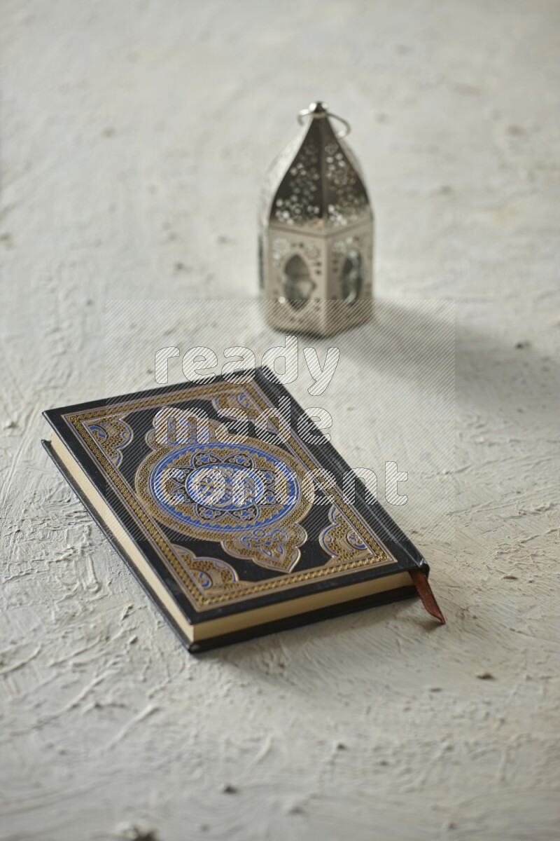 A silver lantern with different drinks, dates, nuts, prayer beads and quran on textured white background