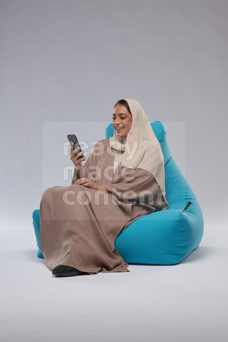 A Saudi woman sitting on a blue beanbag and texting on phone