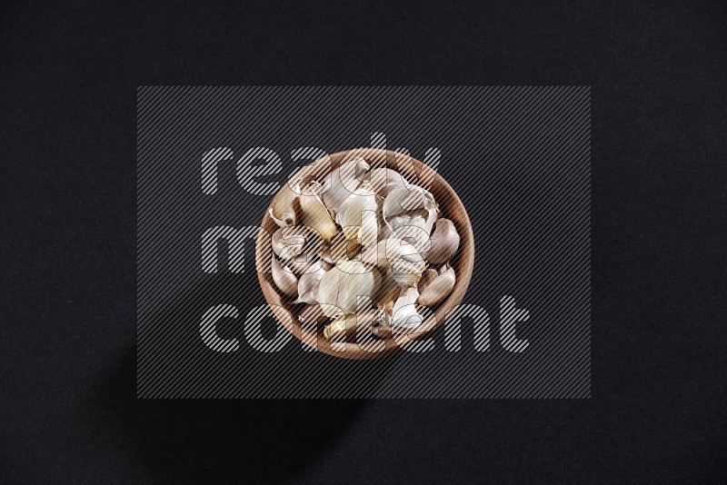 A wooden bowl full of garlic cloves on a black flooring in different angles