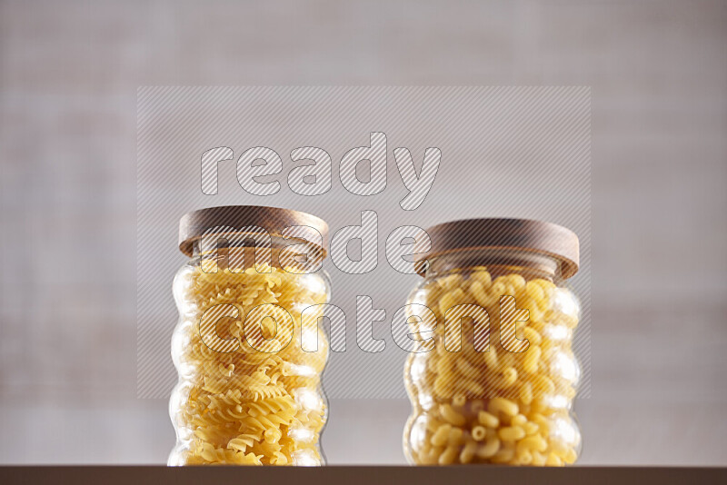 Raw pasta in glass jars on beige background