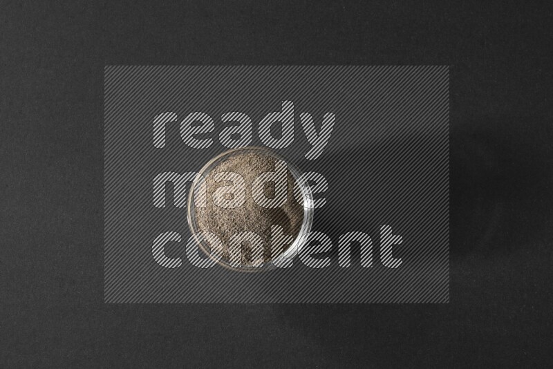 فلفل أسود مطحون في وعاء زجاجي علي خلفية سوداء