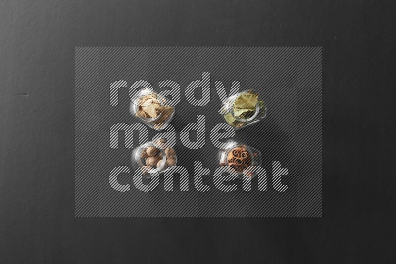 أوراق الغار وزنجبيل مجفف وقرفة وجوزة الطيب في أوعية زجاجية علي خلفية سوداء