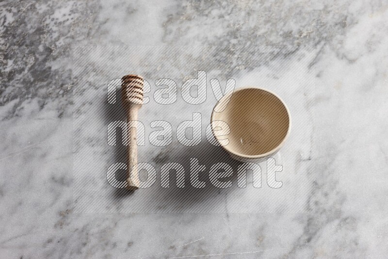 Beige pottery bowl with wooden honey dipper on the side on grey marble background