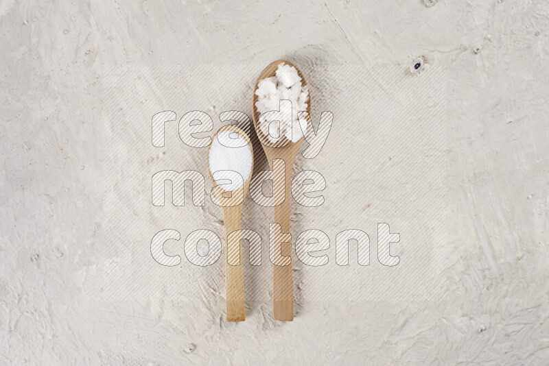 2 wooden spoons filled with fine and coarse salt on white background