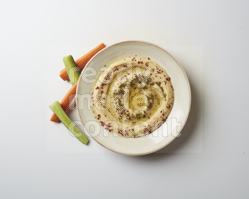 Hummus in a pottry plate garnished with zaatr & sumak on a white background