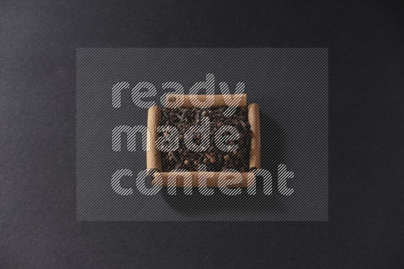 A single square of cinnamon sticks full of cloves on black flooring