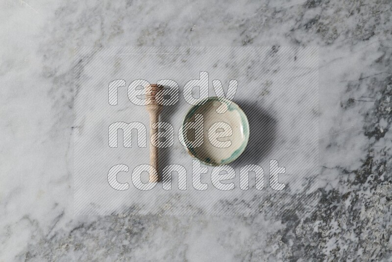 Multicolored pottery bowl with wooden honey dipper on the side on grey marble background