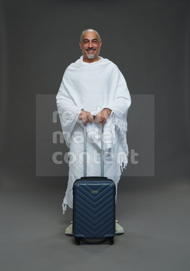 A man wearing Ehram Standing holding traveling bag on gray background