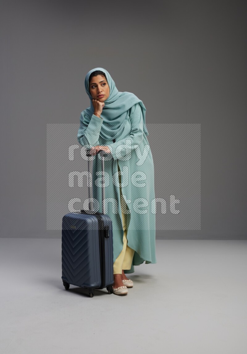Saudi Woman wearing Abaya standing holding Travel bag on Gray background