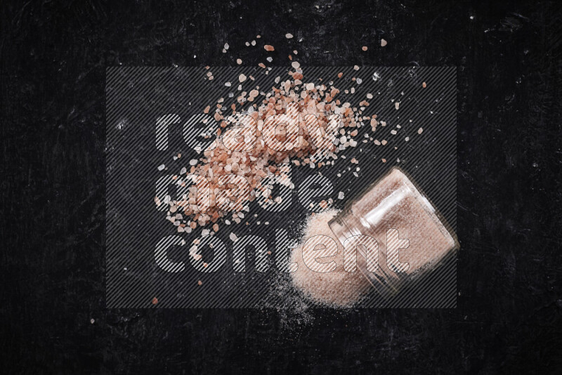 A glass jar full of fine himalayan salt with some himalayan crystals beside it on a black background