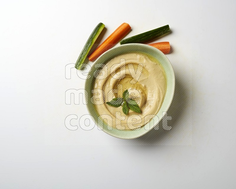 Hummus in a green plate garnished with mint on a white background