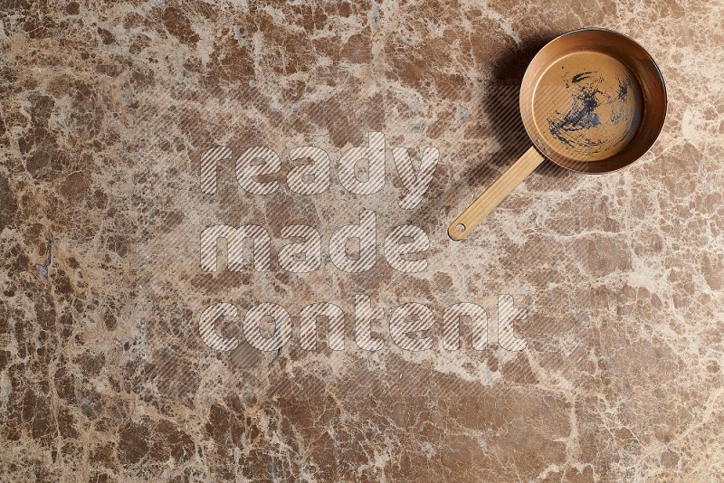 Top View Shot Of A Small Copper pan On beige Marble Flooring