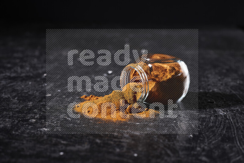 A glass jar full of ground paprika powder flipped with some spilling powder on black background