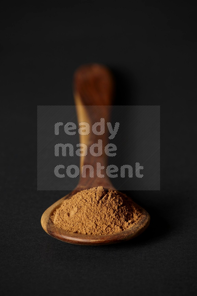 Cinnamon powder in a spoon ladle on black background