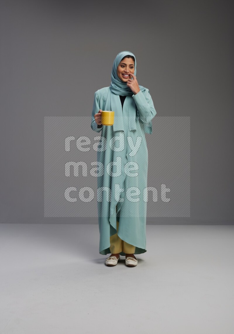 Saudi Woman wearing Abaya standing  holding a mug on Gray background