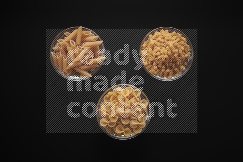 Different pasta types in glass bowls on black background