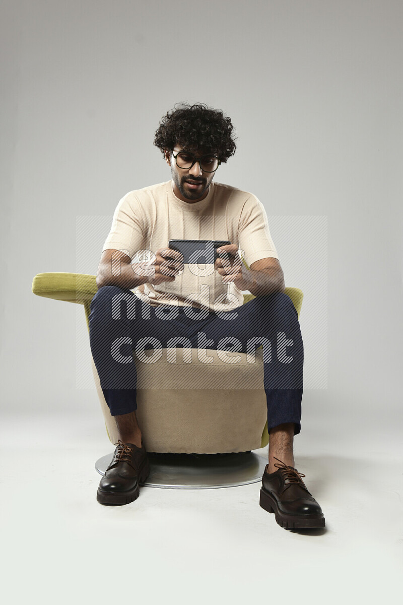 A man wearing casual sitting on a chair gaming on the phone on white background