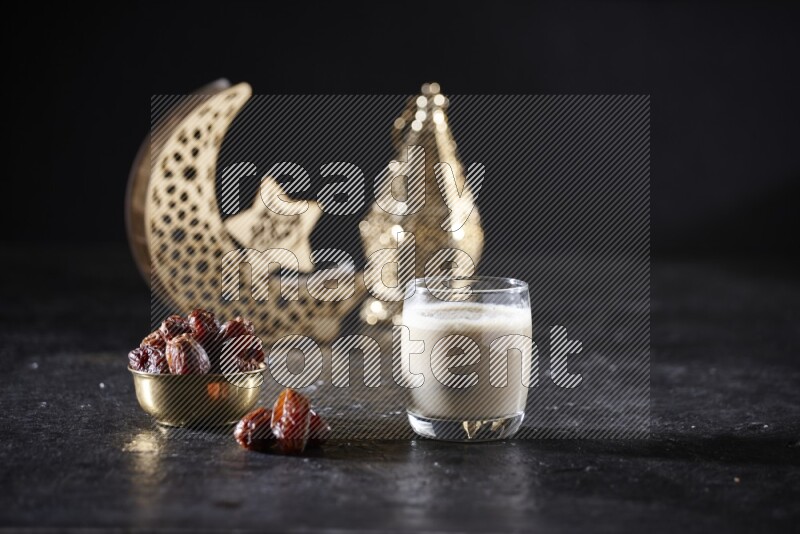 Dates in a metal bowl with dates smoothie beside golden lanterns in a dark setup