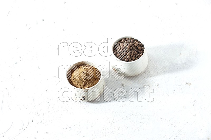 2 beige bowls, one full of allspice powder and the other full of whole balls on a textured white flooring