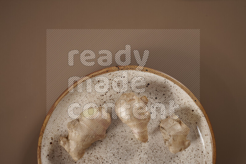 An assorted whole spices on a flat beige plate including fresh and dried ginger, cinnamon sticks, cardamom, turmeric fingers, cloves, star anise on a beige background