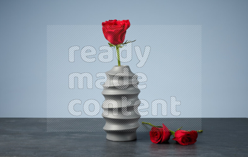 An arrangement of vivid red roses in a grey spiral vase on black marble background