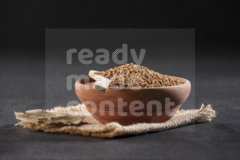 A wooden bowl and spoon full of mustard seeds on a piece of burlap on a black flooring in different angles