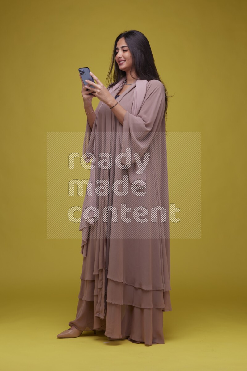 A woman Texting on a Yellow Background wearing Brown Abaya