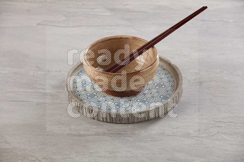 multi color pottery round bowl on top of multi color round ceramic plate and chopsticks, on grey textured countertop