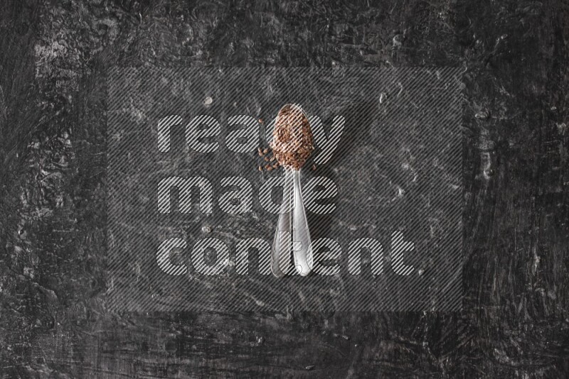 2 metal spoons full of flaxseeds on a textured black flooring