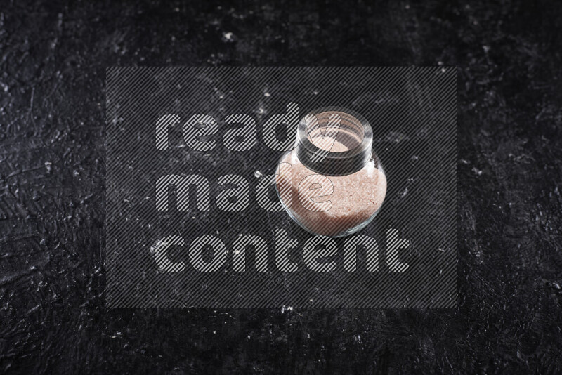 A glass jar full of fine himalayan salt on black background