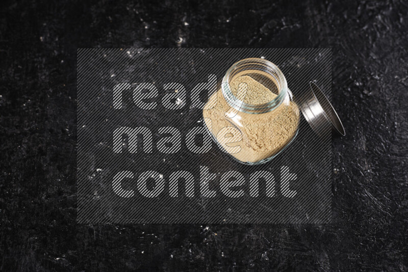 A glass jar full of ground ginger powder on black background