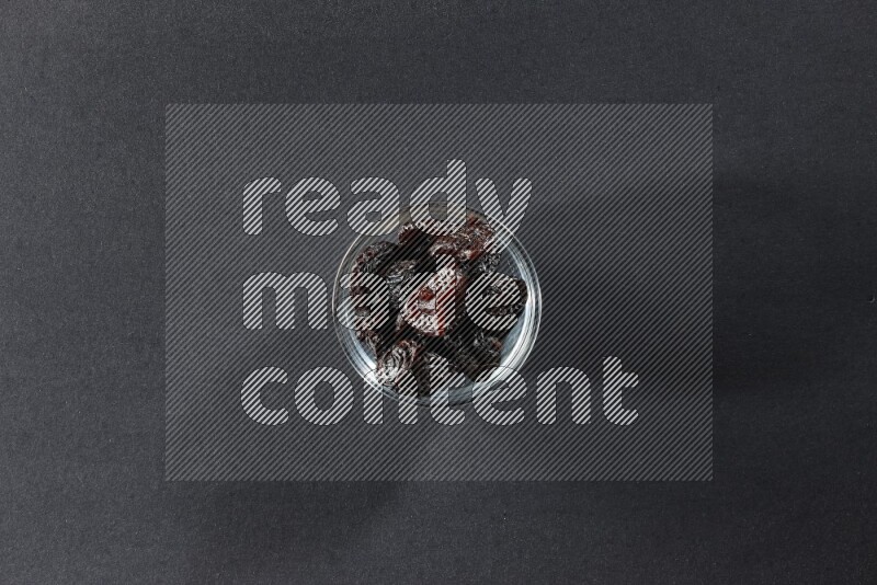 A glass bowl full of dried plums on a black background in different angles