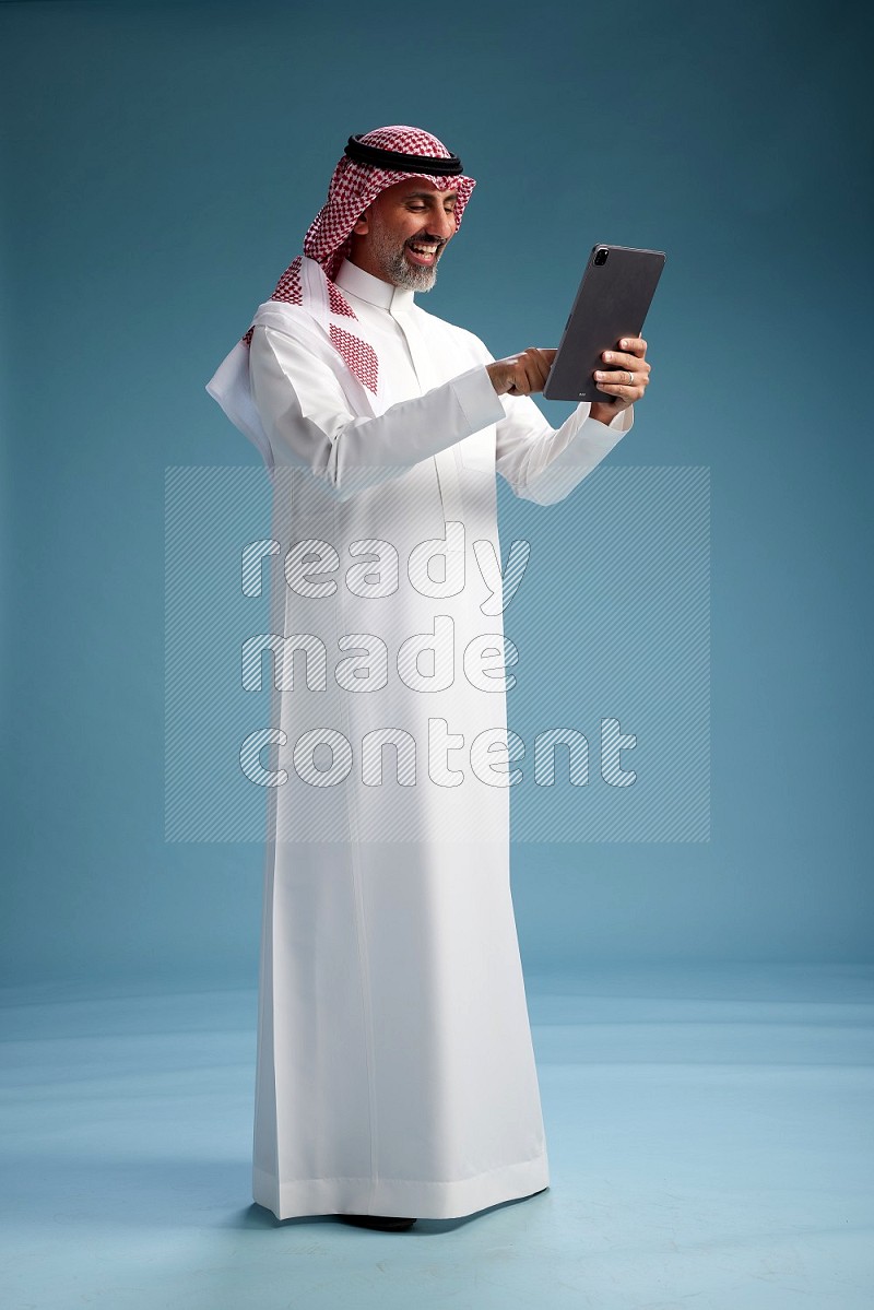 Saudi man wearing thob and shomagh with tablet on Blue background