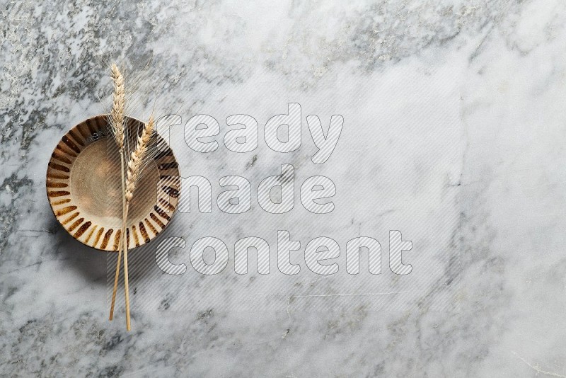 Wheat stalks on Multicolored Pottery Plate on grey marble flooring, Top view