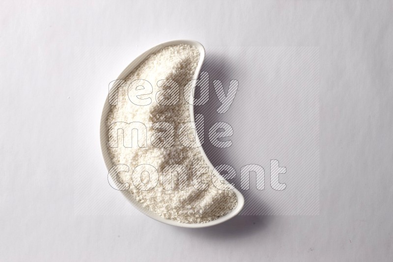 Desiccated coconuts in a crescent pottery plate on white background
