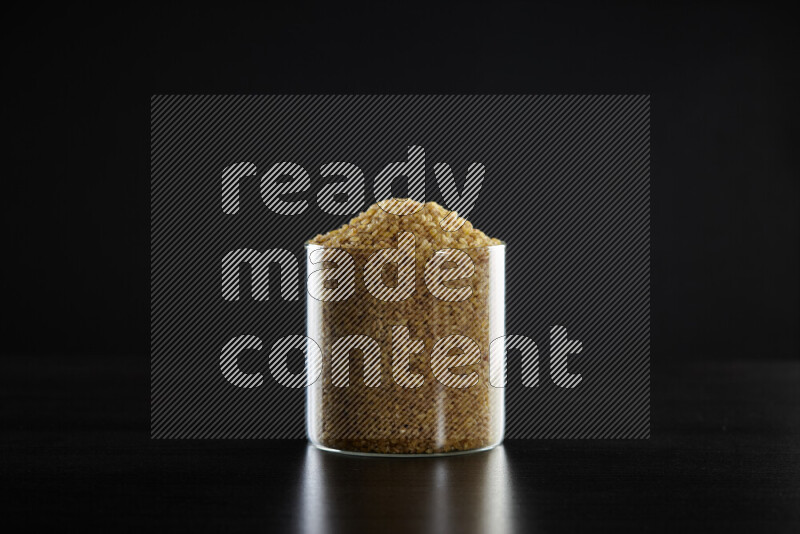 Coarse bulgur in a glass jar on black background