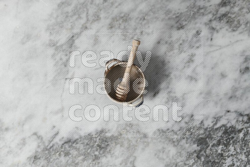 Multicolored pottery bowl with wooden honey dipper in it on grey marble background